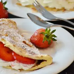 Pyszny omlet z białek z bitą śmietaną i truskawkami, posypany cukrem pudrem i płatkami migdałów.