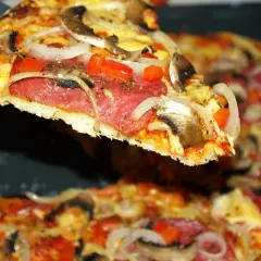 Kawałek pysznej pizzy salami z pieczarkami i cebulą, unoszący się nad resztą zapiekanki.