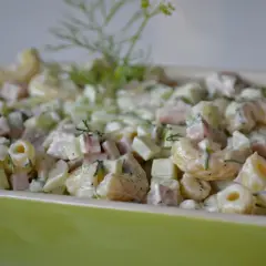 Pyszna sałatka z makaronem, szynką, ogórkiem i serem, udekorowana świeżym koperkiem.