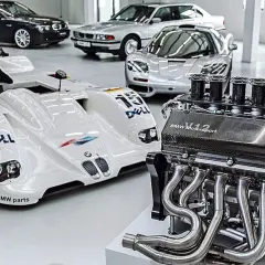 Silnik V12 BMW Motorsport obok białego bolidu wyścigowego i kilku klasycznych BMW.