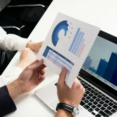 Analityk danych analizuje wykresy i dane na laptopie, omawiając wyniki z kolegą.