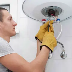 Mężczyzna w żółtych rękawicach dokręca śrubę przy bojlerze. Może to być część instrukcji, jak odpowietrzyć bojler.