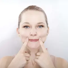 Une femme pratique le yoga du visage, ses doigts pressant ses joues pour un sourire accentué.
