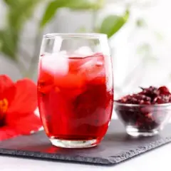 Vaso de agua de jamaica con hielo, flor de jamaica y flor seca. Descubre los agua de jamaica beneficios.