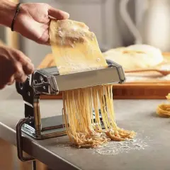 Préparation d'une recette de pâte italienne gastronomique. Une machine à pâtes produit des spaghettis frais, prêts à être cuisinés.