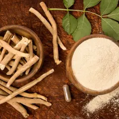 Radici, polvere e capsule di ashwagandha su fondo in legno, con foglie verdi. Ricerca e ashwagandha studi scientifici.