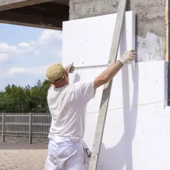 Budowlaniec przykłada styropian do ściany, używając zaprawy klejowej do styropianu.