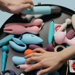 Mani che scelgono tra vari vibratori e sex toys, suggerendo la masturbazione femminile.