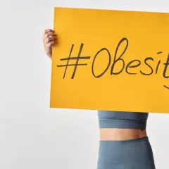 Osoba trzymająca tabliczkę z napisem #Obesity. Problem otyłości w Polsce staje się coraz poważniejszy.