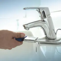 Mano con chiave per cambiare rubinetto lavandino bagno.