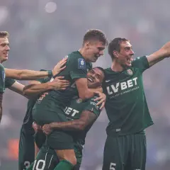 Piłkarze w zielonych koszulkach świętują bramkę, jeden z nich jest niesiony na rękach.