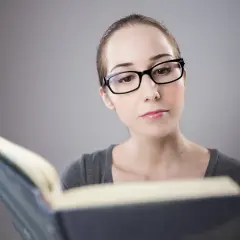 Kobieta w okularach próbuje czytać, jak widzi dyslektyk. Litery tańczą na stronach, tworząc nieczytelny obraz.