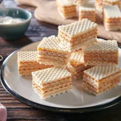 Pyszne wafle z kajmakiem z puszki, ułożone na talerzu. Obok słoiczek z kremowym kajmakiem i miseczka z wiórkami kokosowymi.