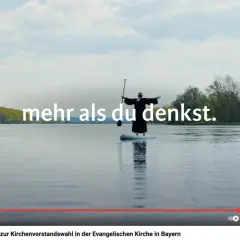 Ein Geistlicher steht auf einem SUP-Board auf einem See. Der Arbeitgeber Kirche bietet mehr als man denkt.