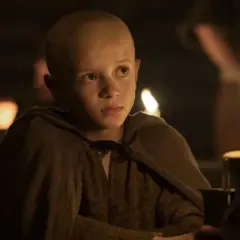 Un jeune garçon chauve, vêtu d'une tunique marron, regarde fixement une bougie allumée. Scène de "A Knight of the Seven Kingdoms Episode 3".