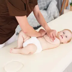 Niemowlę na masażu. Terapeuta wykonuje ćwiczenia metodą Vojty, stymulując rozwój dziecka.