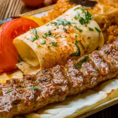 Kebab z mięsa mielonego, grillowanymi warzywami, plackiem i ryżem na talerzu.