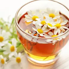Un bicchiere di camomilla per bambini, con fiori freschi che galleggiano nella bevanda dorata.