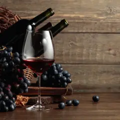 Calice di vino rosso, grappoli d'uva nera e bottiglie in un cesto. Ideale per scoprire i migliori sassicaia abbinamenti.
