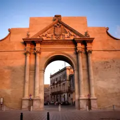 Porta Napoli a Lecce, un maestoso arco in pietra illuminato dal tramonto, accoglie i visitatori con la sua architettura barocca.