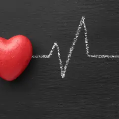 Cuore rosso su lavagna nera con tracciato ECG. Un simbolo di cosa fa alzare la pressione.
