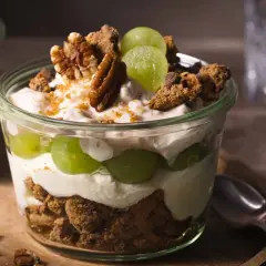 Cremiges Dessert im Glas mit grünen Trauben, zerbröselten Keksen und Nüssen. Ein köstlicher Trauben-Cookie-Dessert-Genuss.