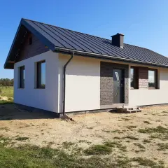 Nowy dom szkieletowy pod klucz, z szarym dachem i białym tynkiem, czeka na wykończenie.