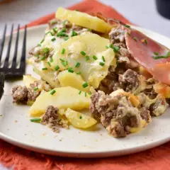 Zapiekanka ziemniaczana z mięsem mielonym, posypana szczypiorkiem, na talerzu z widelcem.