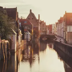 En kanal i Brygge, Belgien, med gamla tegelhus och en bro. Solen går ner och reflekteras i vattnet.