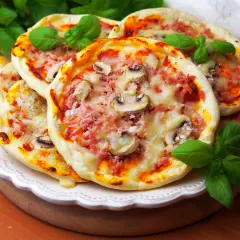 Szybkie mini pizze z szynką i pieczarkami, ozdobione świeżą bazylią, kuszą apetycznym wyglądem.