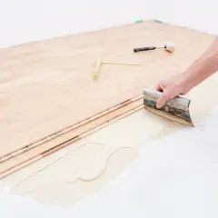 Pose d'un plancher bois étage : application de colle avec une spatule sur le support avant la pose des lames.