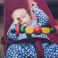Sover gott i sin babysitter elektrisk, med färgglada träpärlor som leksak.