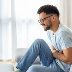 Mężczyzna z okularami cierpi na ból brzucha. Szuka domowych sposobów na ból brzucha, by poczuć ulgę.