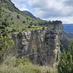 Impresionante pared rocosa del salt de sallent, con vegetación verde y un cielo nublado.