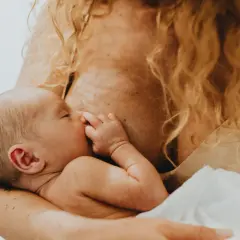 Nowe życie w ramionach mamy. Dziecko w pozycji do karmienia na brzuchu, spokojnie ssie pierś.