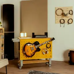 Kreative hobbykeller ideen: Gitarren, Kopfhörer und Kabel sind ordentlich an einer gelben Werkbank mit Lochwand befestigt. Akustikpaneele und weitere Instrumente schaffen eine musikalische Atmosphäre.