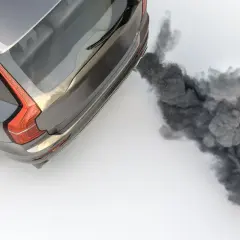 Un coche emite una densa nube de humo negro por el tubo de escape al acelerar, contaminando el aire.