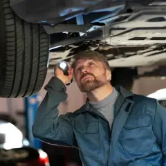 Mechanik z latarką bada podwozie auta, szukając usterki. Czy to jarzmo zawieszenia wymaga wymiany?
