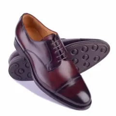 Eleganckie męskie buty ze skóry w kolorze koniaku. Widoczne różne rodzaje podeszwy w butach: skórzana i gumowa z charakterystycznym wzorem.