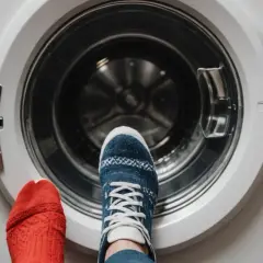 Stojąc przed otwartą pralką, zastanawiasz się, w jakiej temperaturze prać skarpetki. Jedna stopa w czerwonej skarpetce, druga w niebieskiej z wzorem.