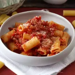 Pyszne rigatoni amatriciana, bogato polane sosem pomidorowym z guanciale i posypane parmezanem, w białej misce.
