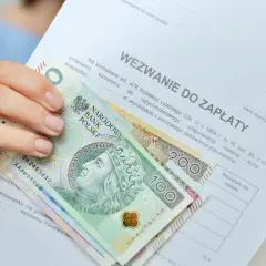 Dłoń trzyma wezwanie do zapłaty i polskie banknoty. Czy to odpowiedź na pytanie, ile zarabia komornik?