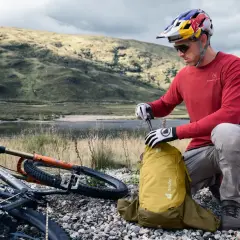Rowerzysta w kasku przygotowuje żółty plecak Deuter, idealny na wycieczkę. Jaki plecak na rower wybrać? Ten wygląda na praktyczny.