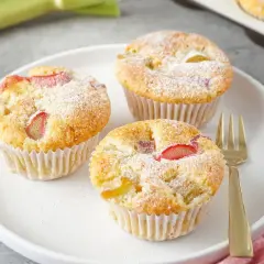 Saftige rhabarber muffins mit joghurt, bestäubt mit Puderzucker, auf einem Teller mit einer goldenen Gabel.
