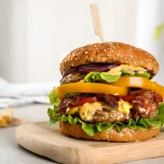 Un délicieux hamburger au barbecue, garni de bacon croustillant, de fromage fondant et de légumes frais, servi sur une planche en bois.