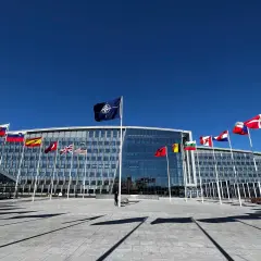 Przed budynkiem NATO, symbolizującym art. 5 traktatu, powiewają flagi państw członkowskich.