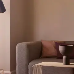 Gemütliches Sofa mit Kissen in mauve farbe, daneben ein moderner Stehlampenfuß und ein Fenster mit zarten Vorhängen.