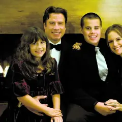 John Travolta med familjen, inklusive sonen Jett, poserar glatt framför en öppen spis.