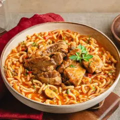 Un reconfortante plato de fideos a la cazuela con costilla, servido en un cuenco rústico, con un toque de perejil fresco.