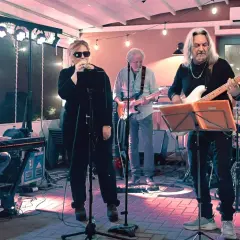 Band di **gruppi musicali piemontesi** in azione: tastierista, cantante, chitarrista, bassista e batterista suonano sotto le luci.
